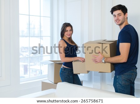 Moving new flat with fun and excitement. Young and beautiful couple is moving to new apartment surrounded with plenty of  boxes. Both are holding packs with their clothes while moving new apartment