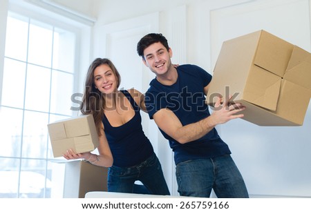 Moving new flat with fun and excitement. Young and beautiful couple is moving to new apartment surrounded with plenty of cardboard boxes. Both are holding packs with open and beautiful smiles