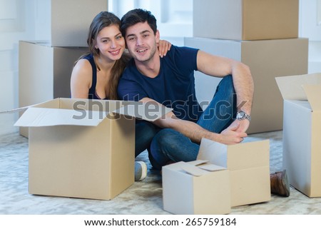 Moving new flat with fun and excitement. Young and beautiful couple is moving to new apartment surrounded with plenty of cardboard boxes. Both are sitting on floor and dreaming about new cozy house