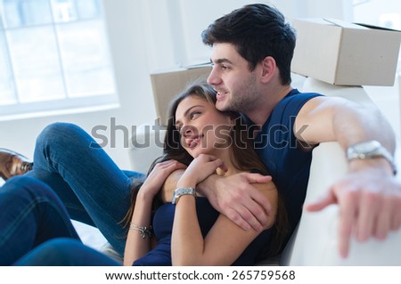 Moving new flat with fun and excitement. Young and beautiful couple is moving to new apartment surrounded with plenty of cardboard boxes. Both are sitting on the sofa and dreaming about new cozy home