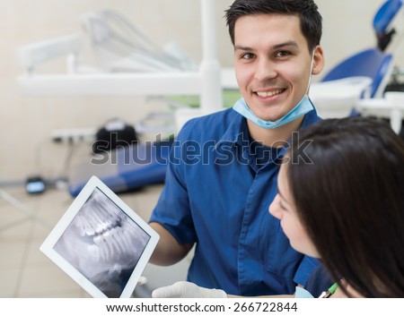 Healthy teeth and dental healthcare. Confident professional doctor dentist is working with pretty female patient. He shows x-ray teeth on tablet. Doctor stomatologist is wearing medical clothing