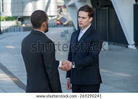 Excellent business agreement. Two confident and motivated businessmen are shaking hands. Both are wearing formal suits. Outdoor business concept