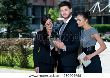 Proper business agreement. Three confident and motivated business partners are looking in tablet and discussing issues of business project. All are wearing formal suits. Outdoor business concept