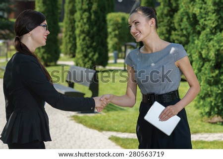 Excellent business agreement. Two confident and motivated business woman are shaking hands. Both are wearing formal suits. Outdoor business concept