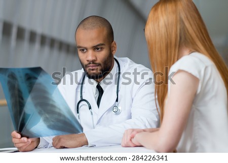 Doctor is examining x-ray in a hospital. Portrait of confident and professional doctor therapist wearing white medical clothes with his patient. Medical hospital concept.