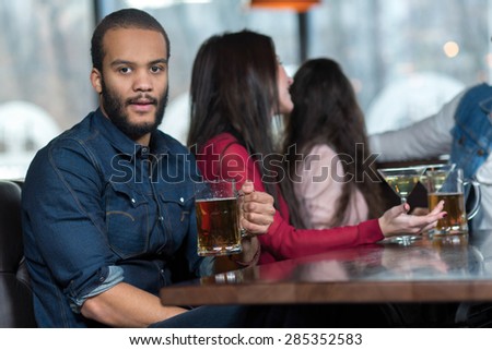 Perfect beer party in a pub. Portrait of handsome man in a pub. Man is drinking beer and smiling. His friends are on the background. Beer pub football concept