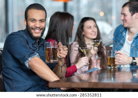 Perfect beer party in a pub. Portrait of handsome man in a pub. Man is drinking beer and smiling. His friends are on the background. Beer pub football concept