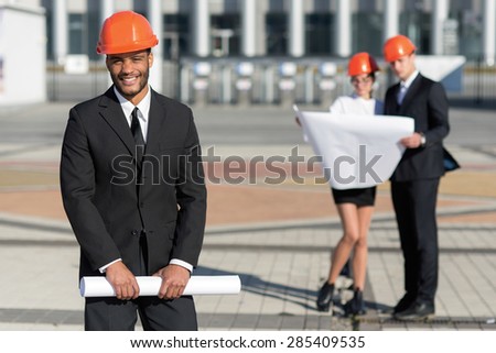 New building project. African architect in protective helmet is looking at the camera with a smile. Business architects concept
