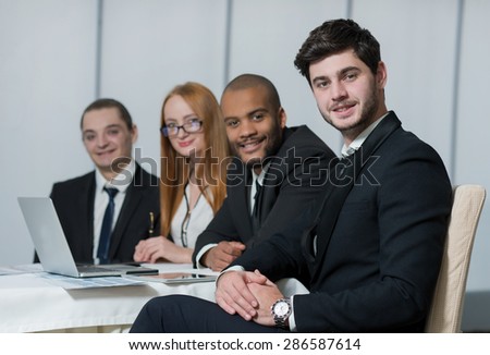 Well done business project. Portrait of confident and motivated businessman working on the project with his team with a smile. All are wearing formal suits. Office business concept