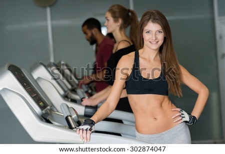 Great training result. Young and pretty woman is having training on treadmill. Her friends are on treadmills on the background. Active workout in a gym. Healthy sportsmen concept