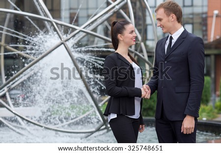 Business agreement. Two  confident motivated business partners are working on the project. Both  are wearing formal suits. Outdoor business concept. Their motivated colleagues are on the background