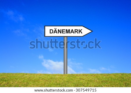 White signpost on green grass showing Denmark in german language in front of blue sky