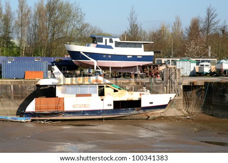 Boat waiting for repair in muddy dock and repaired boat on quayside.