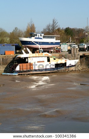 Boat waiting for repair in muddy dock and repaired boat on quayside.