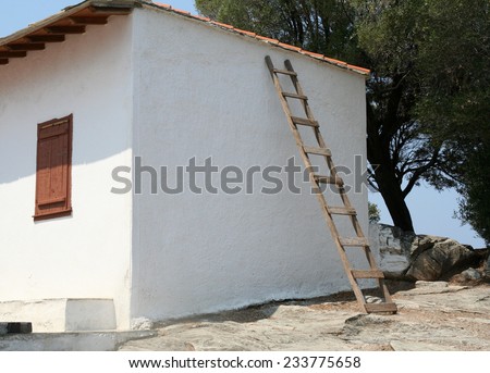 Ladder against a wall. An unsecured ladder leaning against a wall of a small whitewashed house in Greece. Shows health and safety issues and country ways as well as house maintenance.