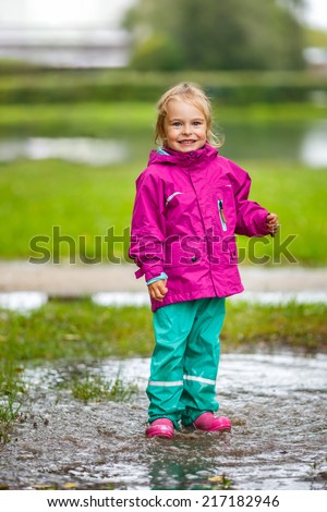 Happy little girl stays in a puddle