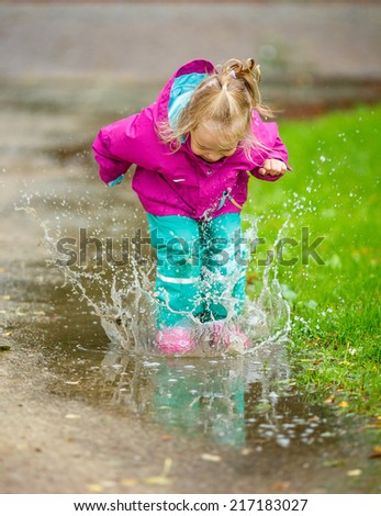 Happy little girl jumps into a puddle