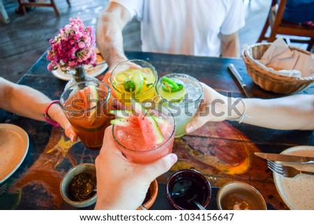 Friends toasting, saying cheers holding tropical blended fruit drinks