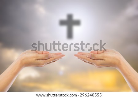 Hands of man praying over blurred the cross on the sky background.