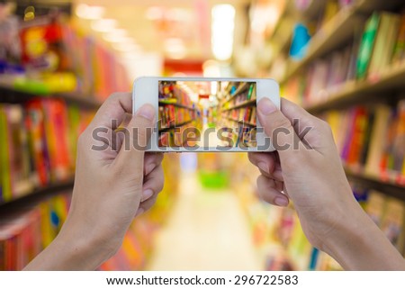 Women hand holding blank mobile smart phone in book store on shelf at shopping center for background usage.