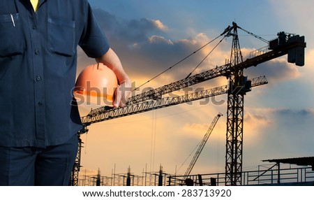 engineer holding orange helmet on background of new office buildings, Silhouette Crane and construction cranes in sunset sky