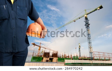 engineer holding orange helmet on background of new office buildings and construction cranes in blue sky