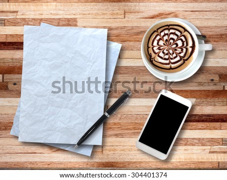 Top view on paper, smartphone, pen and cup of coffee on wooden office desk.