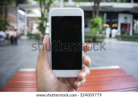 Man\'s hand shows mobile smartphone in vertical position, blurred background - mockup template