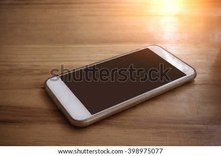 Smart phone with blank screen lying on wooden table- vintage filter effect