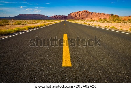 Close up road view of yellow center lines with mountains in distance.