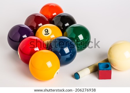 Nine Ball racked in a diamond shape on a plain white background left side with cue stick, chalk and cue ball in foreground.