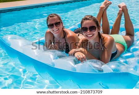 Young female adults smiling and relaxing floating in pool on raft.