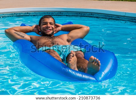 Young adult african-american male lying on raft having fun in swimming pool during summer.