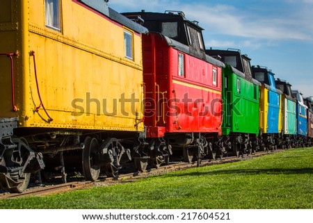 Colorful antique train cars against blue sky with green grass in foreground.