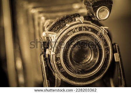 Close up of vintage camera showing lens and bellows with selective focus and sepia filter.
