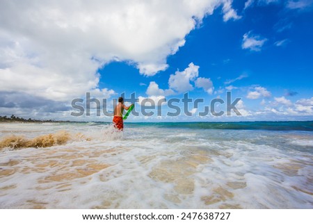Young boy enters the surf with boogie board shot wide angle.