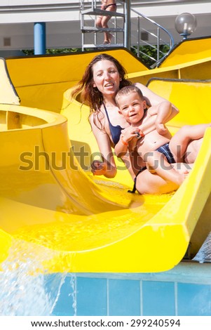 happy child and mom playing with the slide in the pool