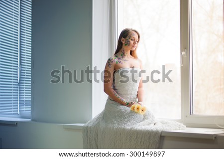 Girl with flower bodyart and sunflowers bouquet and wreath near window