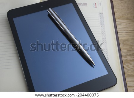 Metal pen,tablet pc and agenda book on wooden background