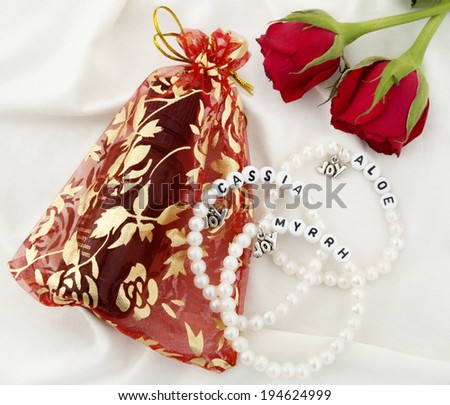 Small bottle of Anointing Oil in Gift Bag, Three Pearl Bracelets and Two Red Roses on White Background