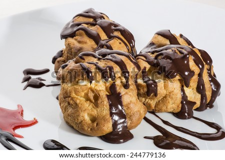 Handcrafted eclairs topped with milk chocolate sauce with cream filling placed over appetizingly decorated plate with chocolate and red sauces