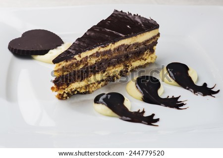 Splendid Opera cake layered with butter cream, sponge cake and chocolate covered in a glaze, placed on decorated plate with cream and drops of dark chocolate and a heart shaped piece of chocolate