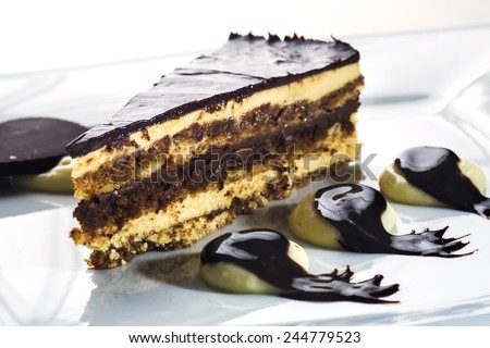 Splendid Opera cake layered with butter cream, sponge cake and chocolate covered in a glaze, placed on decorated plate with cream and drops of dark chocolate and a heart shaped piece of chocolate