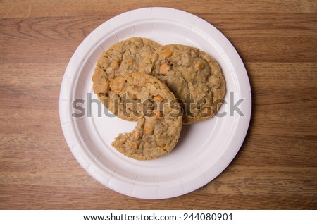 Oatmeal cookies with Butterscotch chips arranged on a paper plate, one cookie bitten into.