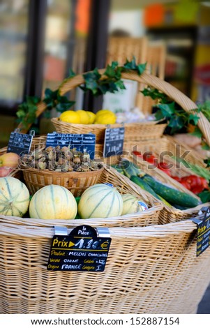 fresh fruit and vegetables in a large woven basket in front of a small shop in france