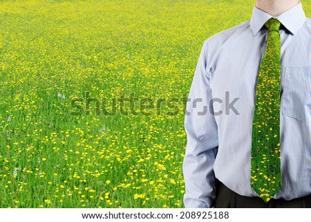 a business man stood in a green field of butter cups with matching tie