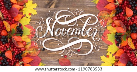 November hand lettering inscription. Bright red autumn leaves and berries frame composition on old wooden background. Great season texture with fall mood. Nature november background.