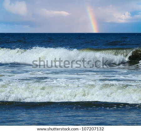 Ocean Waves Breaking on Shore with a Partial Rainbow in the Background