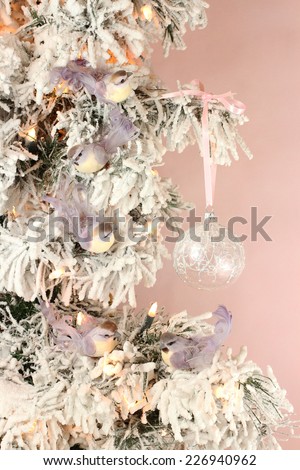 Decoration on Christmas tree - light violet birds and glassy ball on snowy spruce on pink background