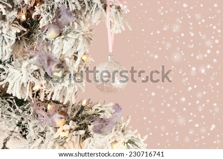 Decoration on Christmas tree - light violet birds and glassy ball on snowy spruce on pink background with snow mist